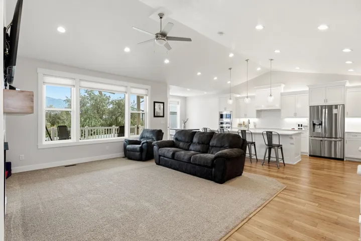 Vaulted ceilings with recessed lighting, large windows, wood-finish flooring, white cabinetry, and stainless steel appliances