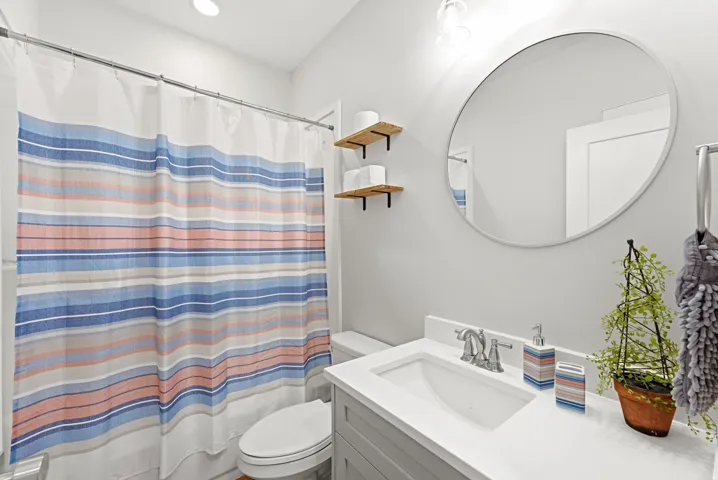 Vanity with a single basin sink, wall-mounted circular mirror, and built-in shelving