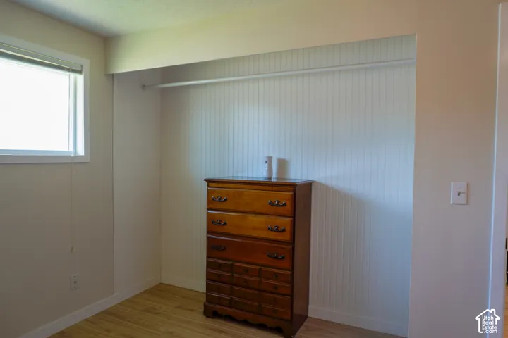 Recessed closet area with beadboard paneling and a hanging rod, complemented by wood-finish flooring and a single window