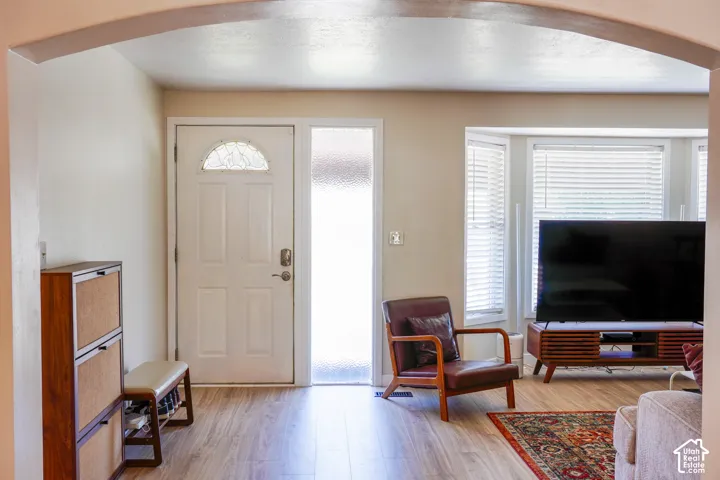 Wood-finish flooring throughout, white paneled entry door with decorative glass transom, frosted sidelight, and a bay window with blinds
