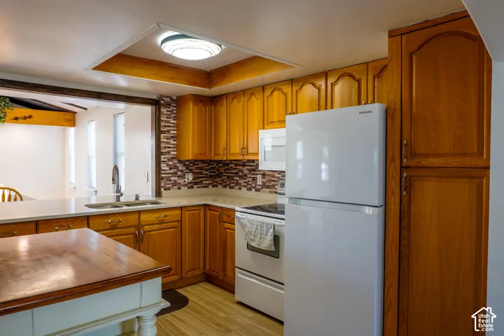 Wood-finish cabinetry, mosaic tile backsplash, double basin sink, white appliances, and wood-finish flooring