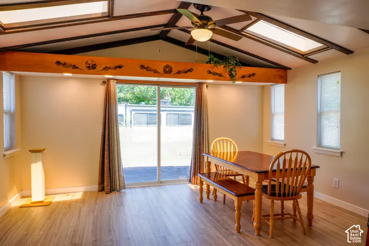 Bright and airy room featuring vaulted ceilings with exposed beams, skylight panels, and a ceiling fan