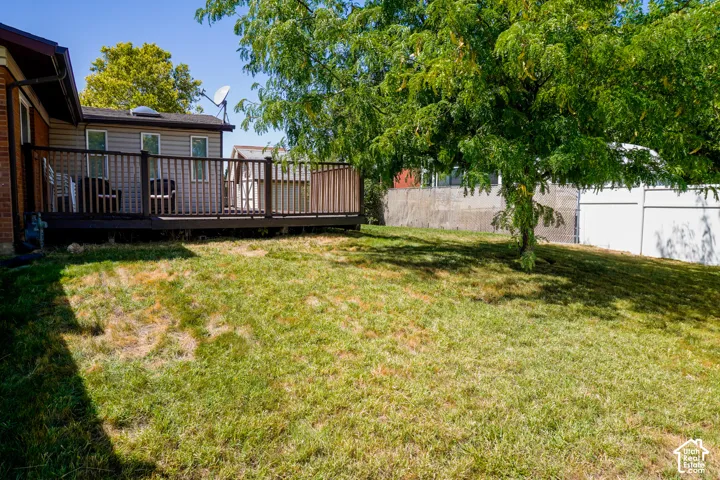 Expansive grassy yard with mature tree coverage, featuring a multi-level wooden deck