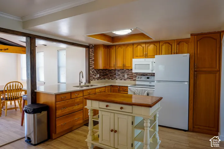 Kitchen featuring wood-finish cabinetry, white appliances, a tile backsplash, and light-toned countertops