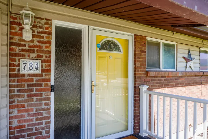 Welcoming brick facade with bright yellow entry door featuring a transom window, complemented by textured glass storm door and stainless steel hardware