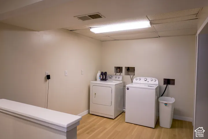 Laundry area featuring wood-finish flooring, drop ceiling, and bright overhead lighting
