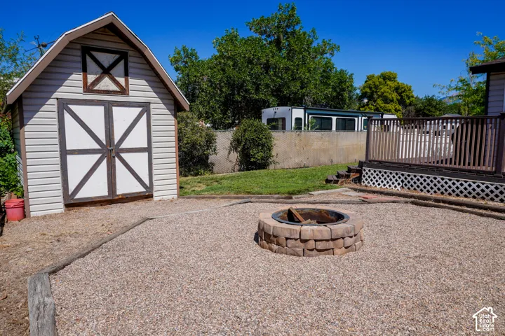 Gravel hardscaping featuring a built-in stone fire pit, a barn-style storage shed with paneled doors, and a wood-decked patio with lattice skirting