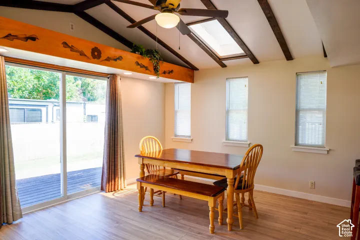 Vaulted ceiling with exposed wood beams, skylight, wood-finish flooring, and sliding glass doors to the exterior