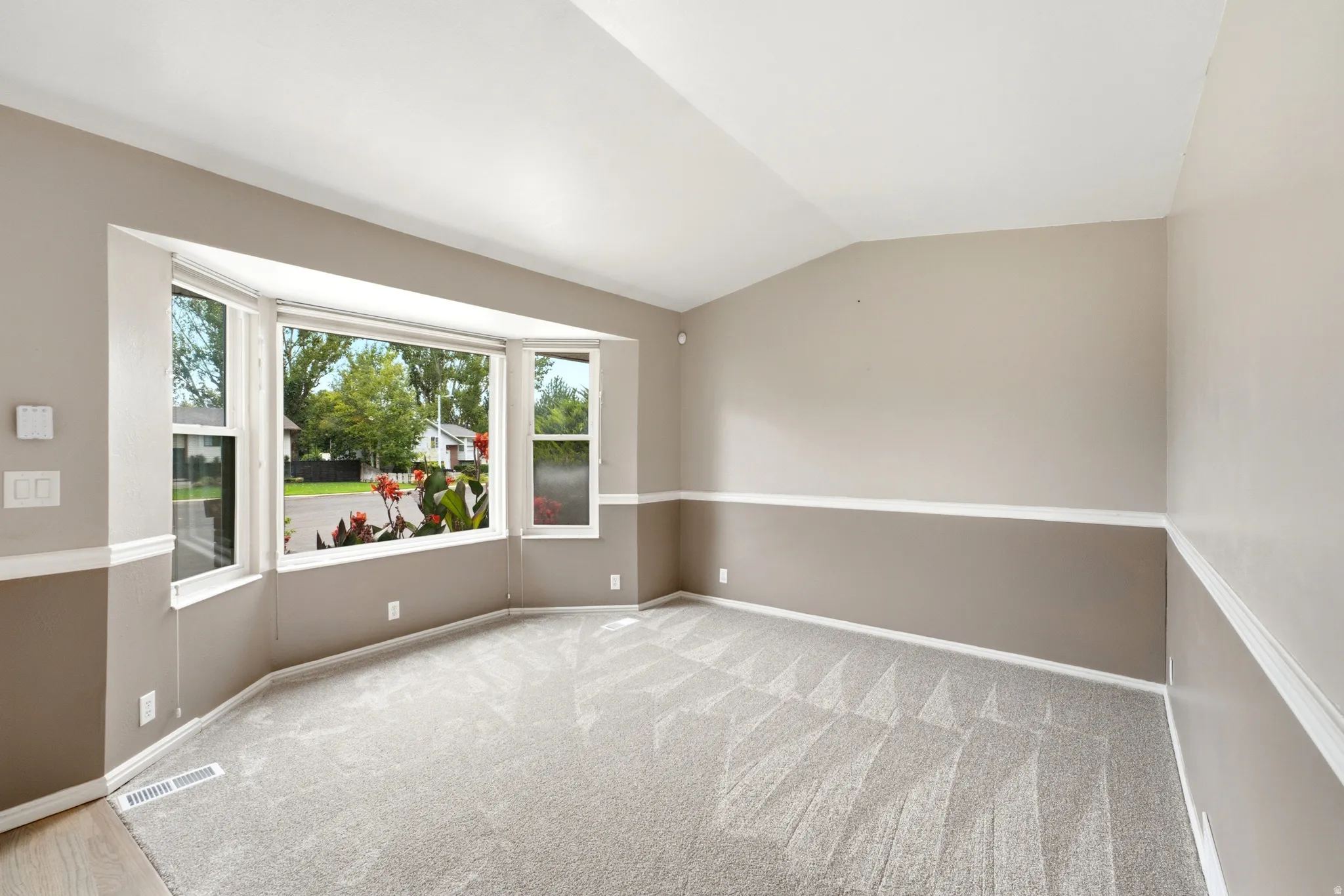 Bay window, two-tone painted walls, wall trim, vaulted ceiling, and patterned carpeting