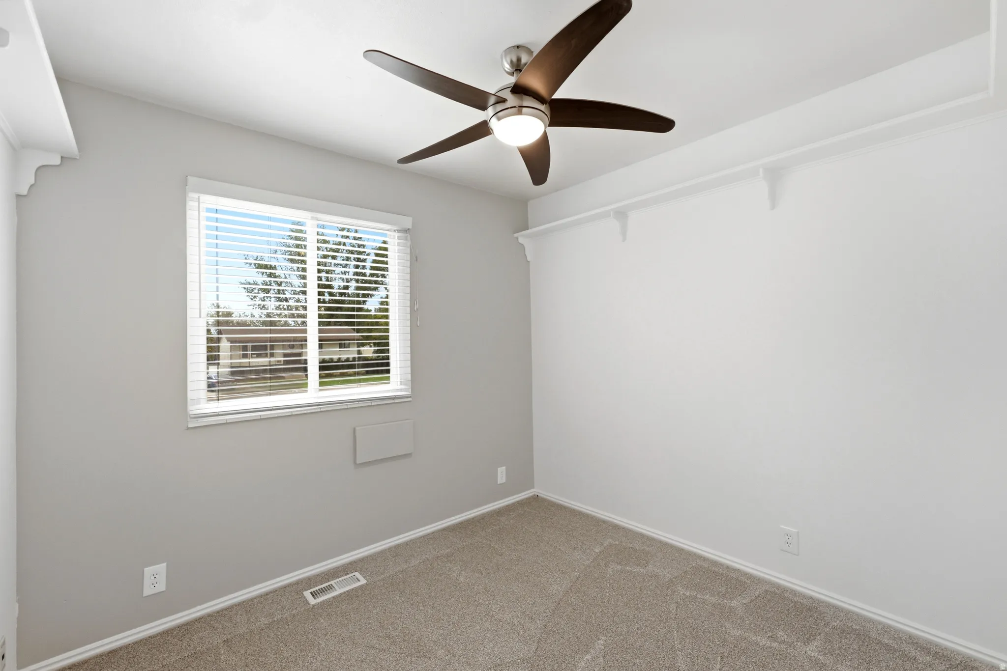 Ceiling fan with integrated lighting, window with horizontal blinds, wall-mounted shelving, and carpeted flooring