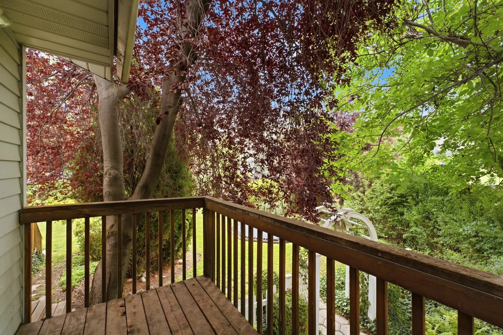 Wood-plank balcony with wood railing, surrounded by mature deciduous trees