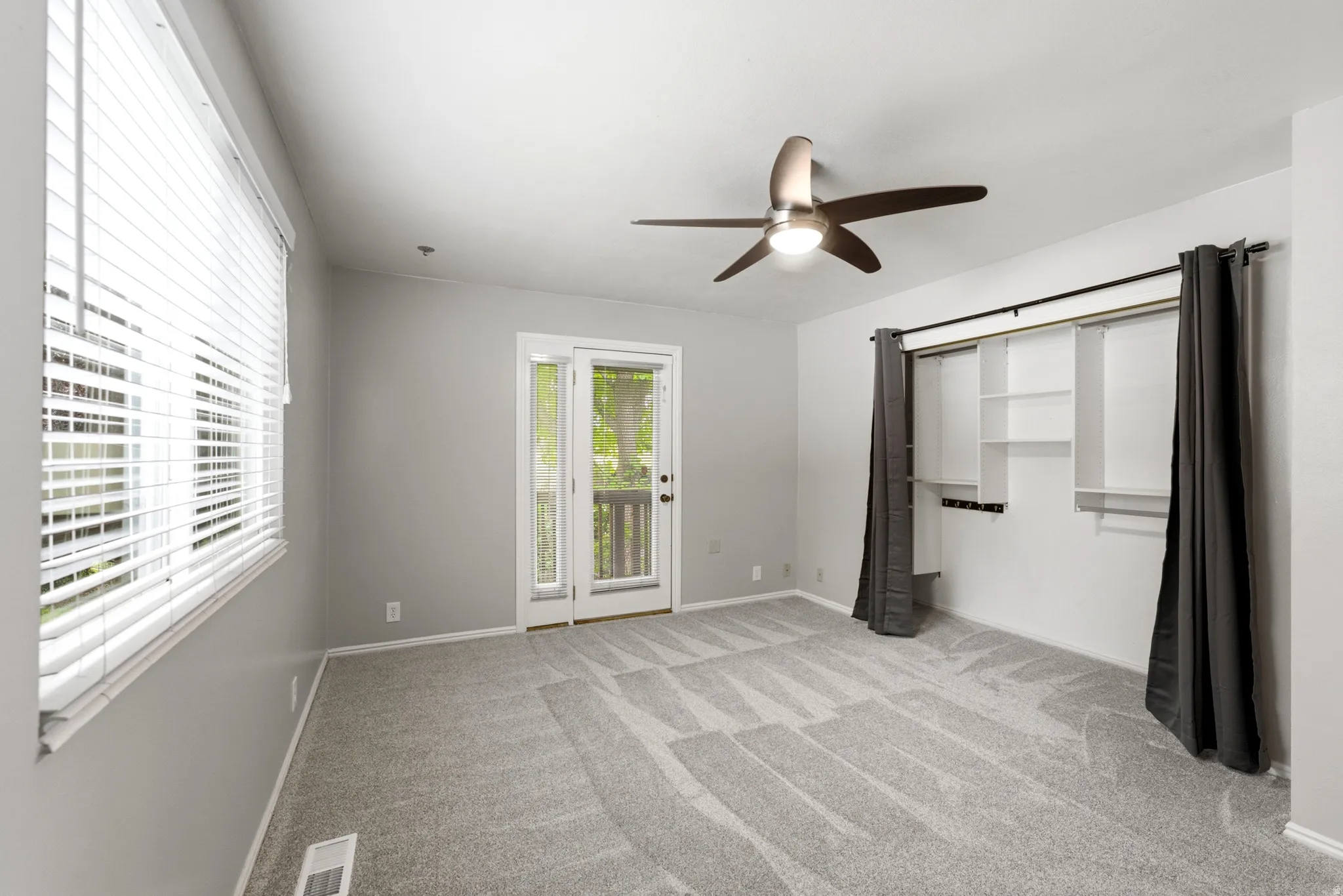 Carpeted room featuring a ceiling fan with integrated lighting, a glass-paneled door, and built-in closet shelving