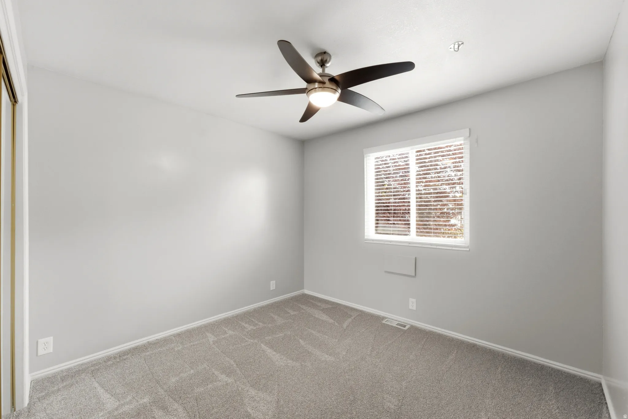 Light gray wall finish, neutral tone carpet, ceiling fan with integrated lighting, window with horizontal blinds, and a built-in sliding door closet