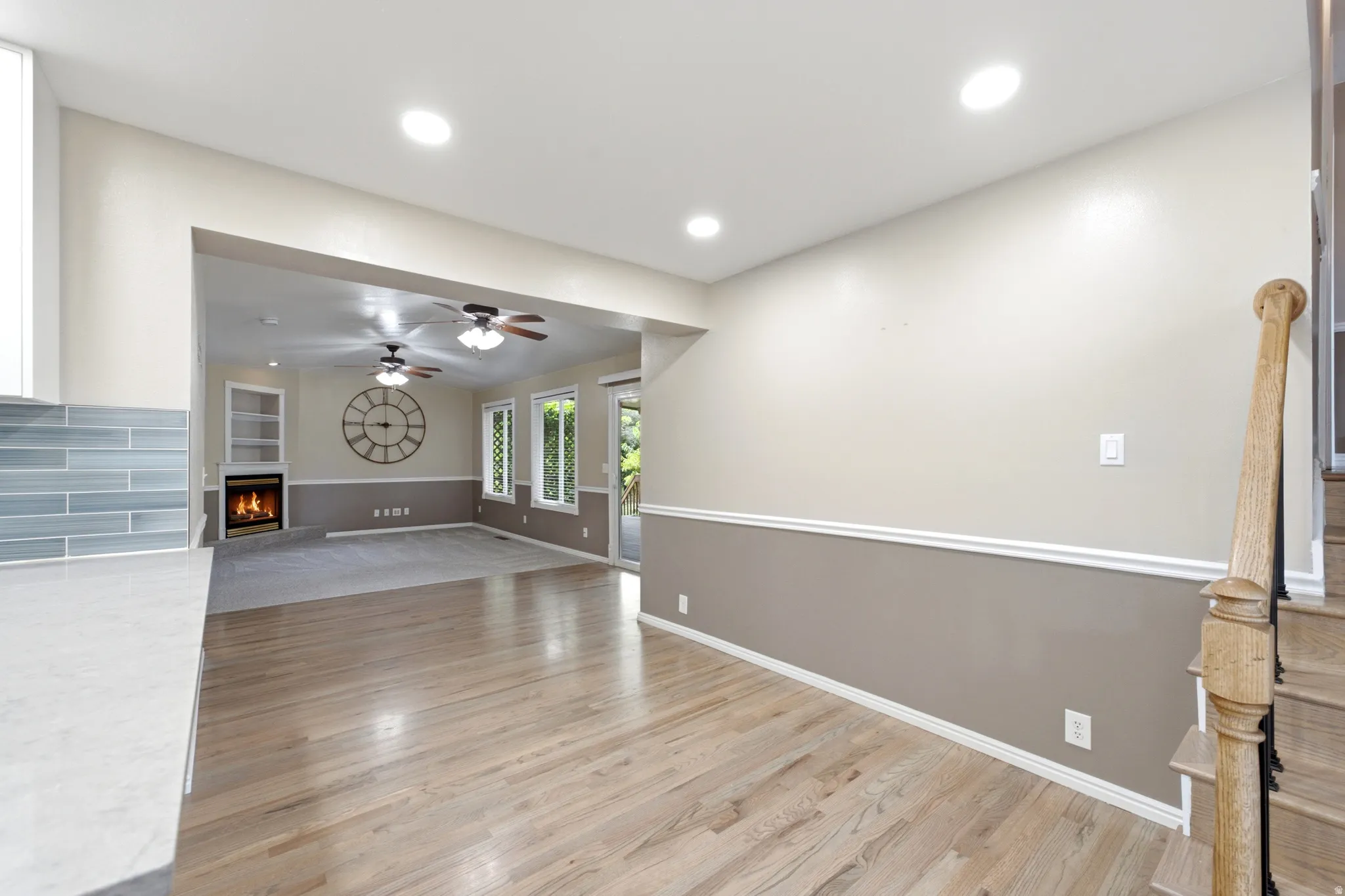 Hardwood flooring, recessed lighting, fireplace with built-in shelving, glass subway tile backsplash, and a wood staircase
