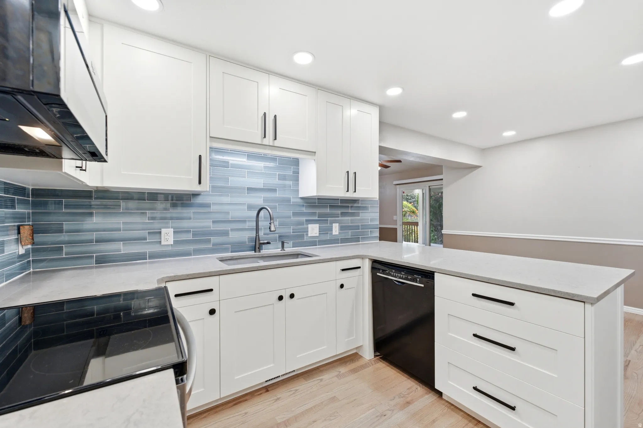 White shaker cabinetry, light-toned countertops, a full suite of black appliances, and recessed lighting