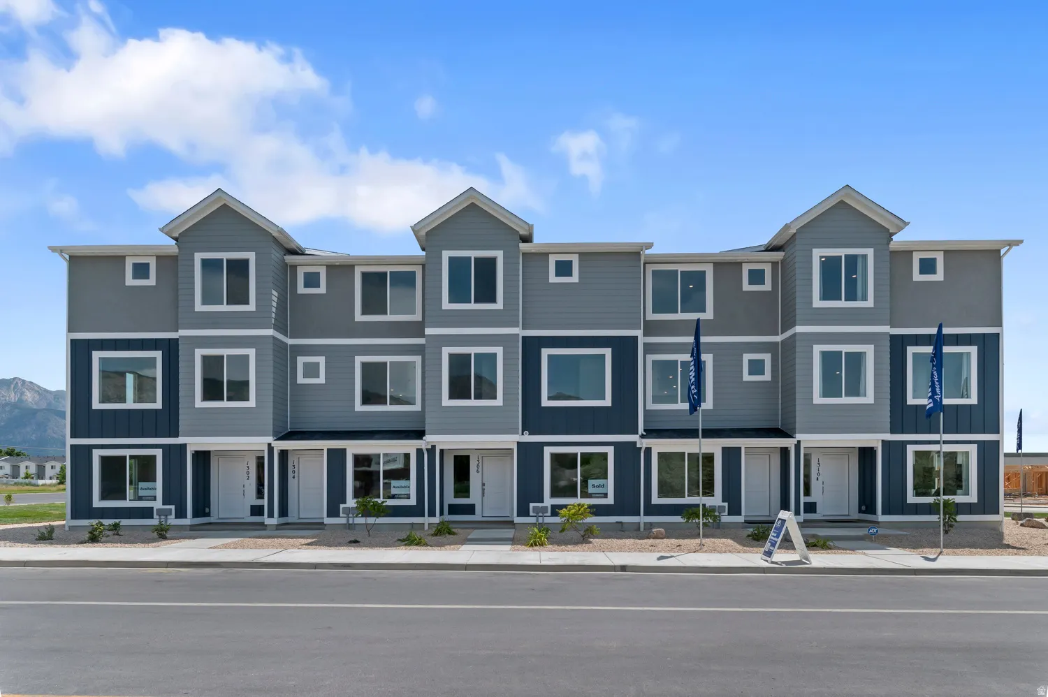 Multi-level townhome exterior featuring varied siding textures, white-framed windows, and a paved sidewalk