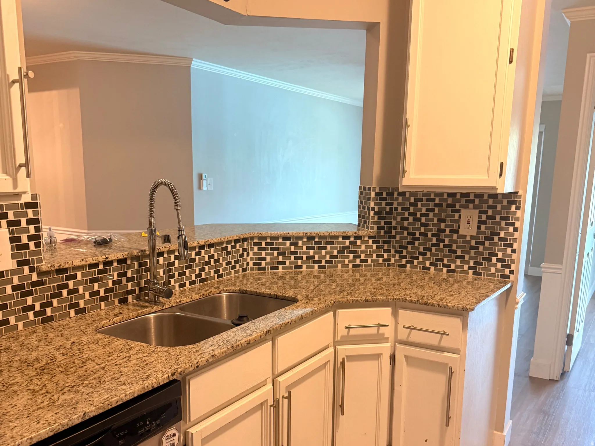 Kitchen featuring a stainless steel double basin sink, pull-down faucet, granite-style countertops, mosaic tile backsplash, and white cabinetry with brushed nickel hardware