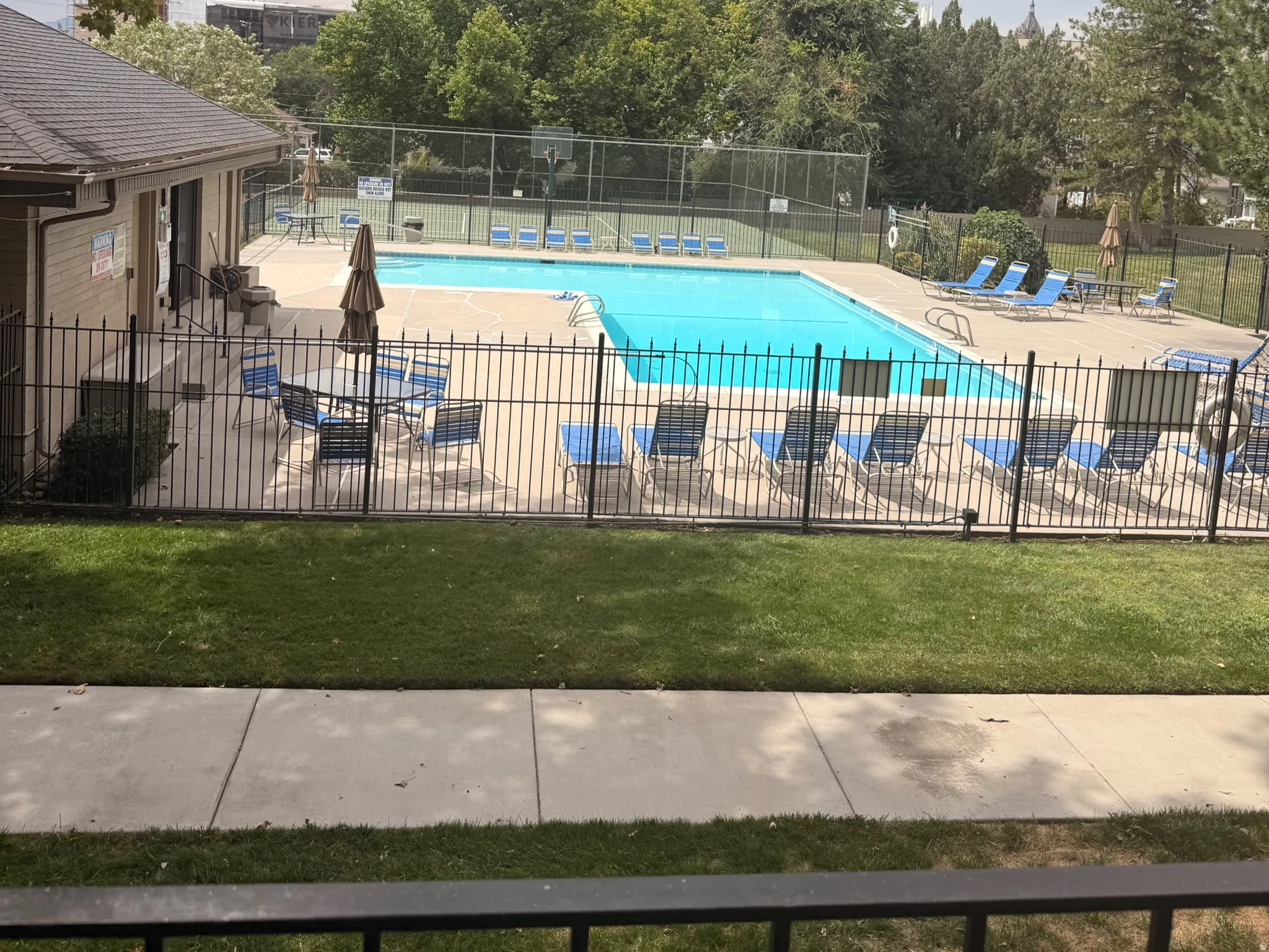 View from the balcony....Fenced swimming pool with a surrounding paved deck, adjacent building, and a green lawn