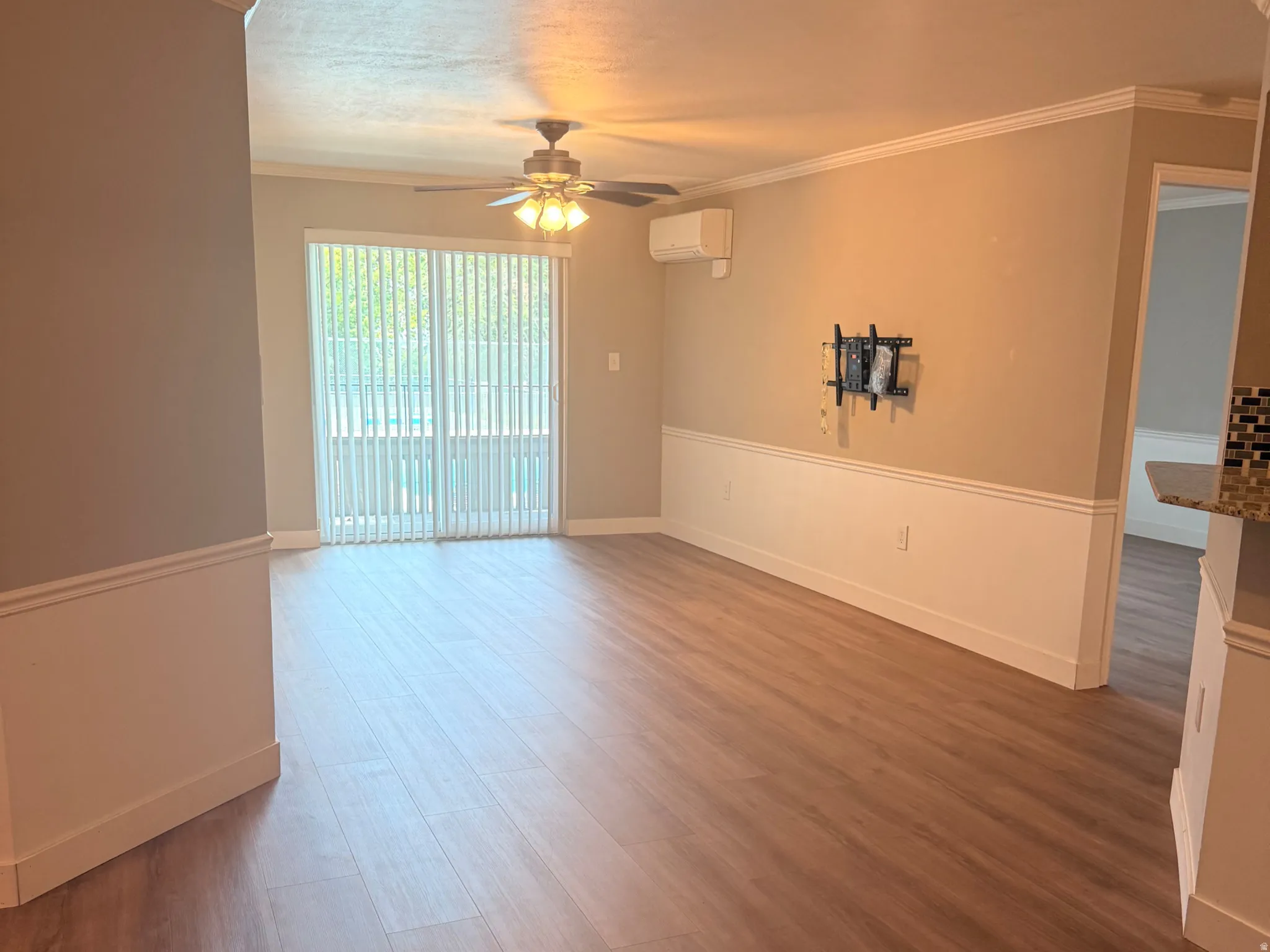 Living room with balcony. Wood-finish flooring, crown molding, chair rail molding, ceiling fan with integrated lighting, and sliding glass door with vertical blinds