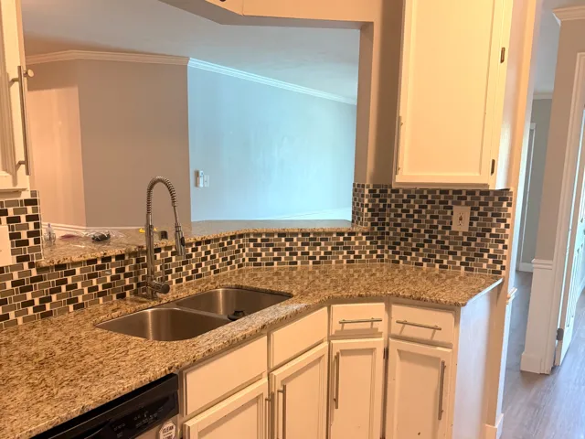 Kitchen featuring a stainless steel double basin sink, pull-down faucet, granite-style countertops, mosaic tile backsplash, and white cabinetry with brushed nickel hardware