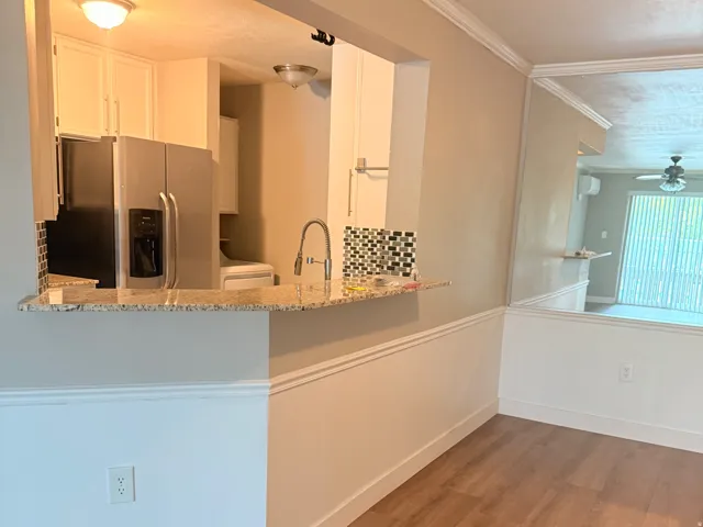 *Fridge is included! Wood-finish flooring, half-wall with wainscoting, granite-style countertop, stainless steel refrigerator, and white cabinetry