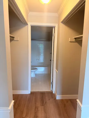 2 Sided closet and bathroom entrance. Wood-finish flooring leading to a full bathroom with a white tile floor and a tub-shower combination