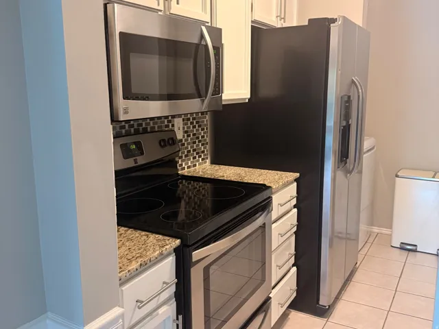 Kitchen featuring white cabinetry, granite-style countertops, stainless steel appliances, mosaic tile backsplash, and tile flooring