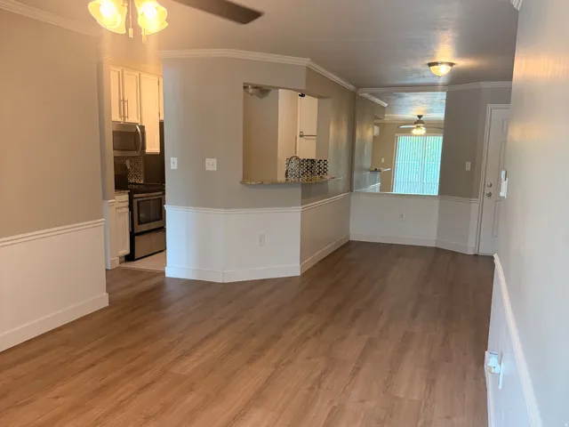Living room to kitchen. Wood-finish flooring throughout, two-tone wall treatment, and an open pass-through kitchen with white cabinetry