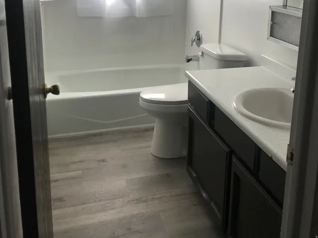 Wood-finish flooring, white vanity with integrated sink, white bathtub, built-in shelving, and a window