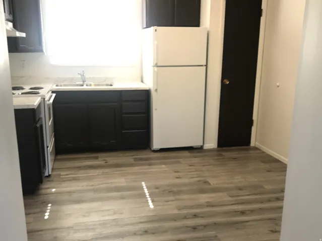 Kitchen featuring dark wood-finish cabinetry, white countertops, a stainless steel sink, and wood-finish flooring