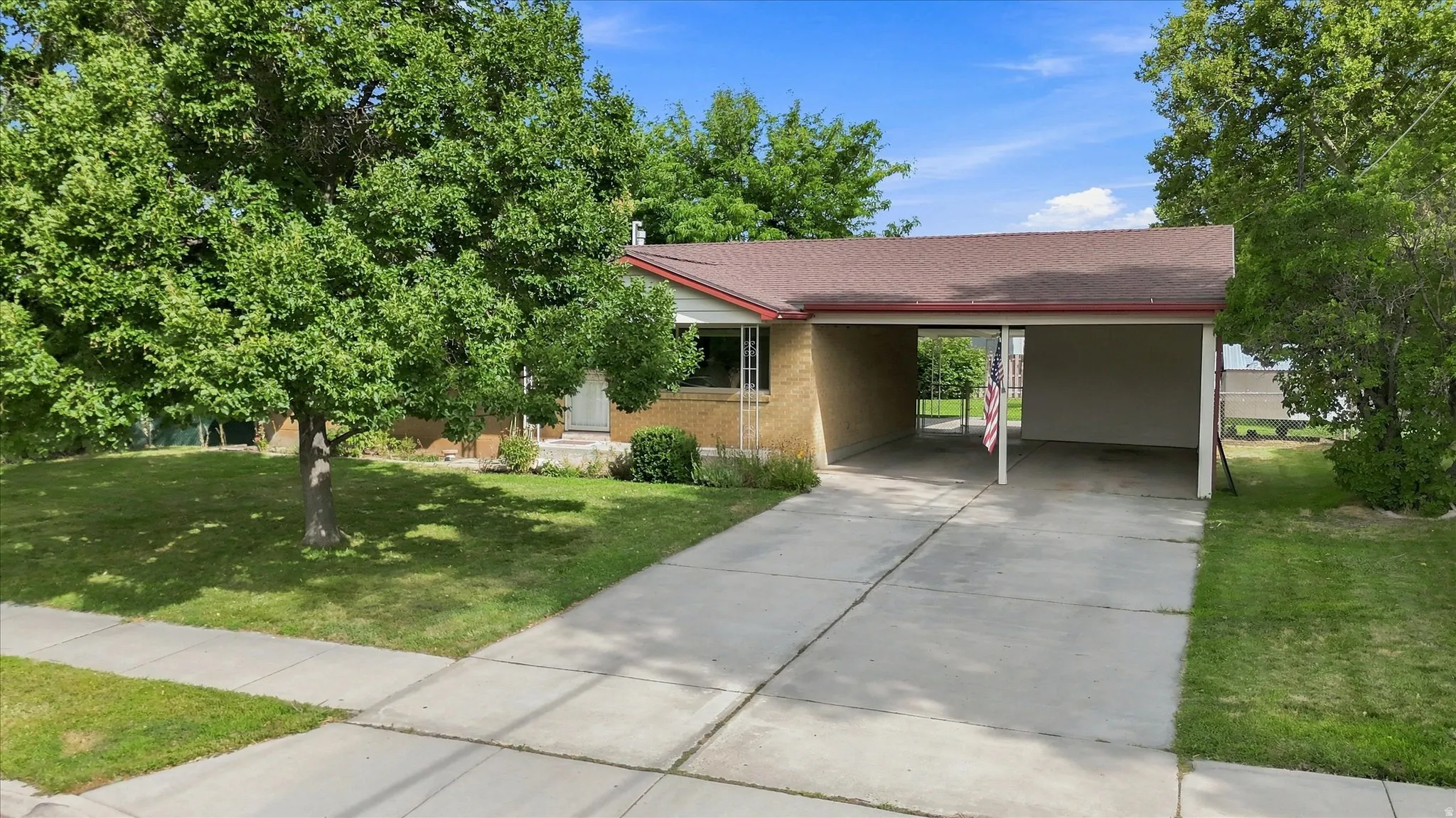 Attached carport with a concrete driveway, mature trees, and a front lawn