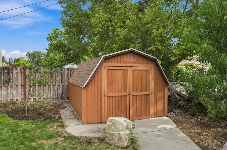 Wood-sided storage shed with a gambrel roof, double doors, and a concrete pathway