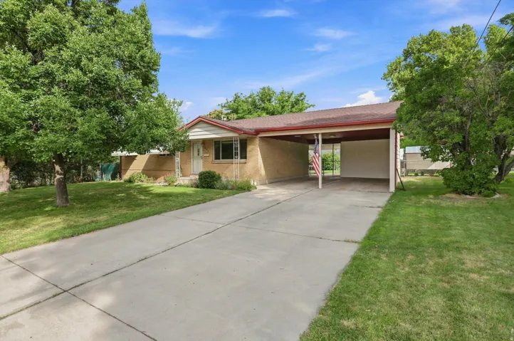 Expansive paved driveway leading to a covered carport, manicured lawn with mature trees, and a brick facade