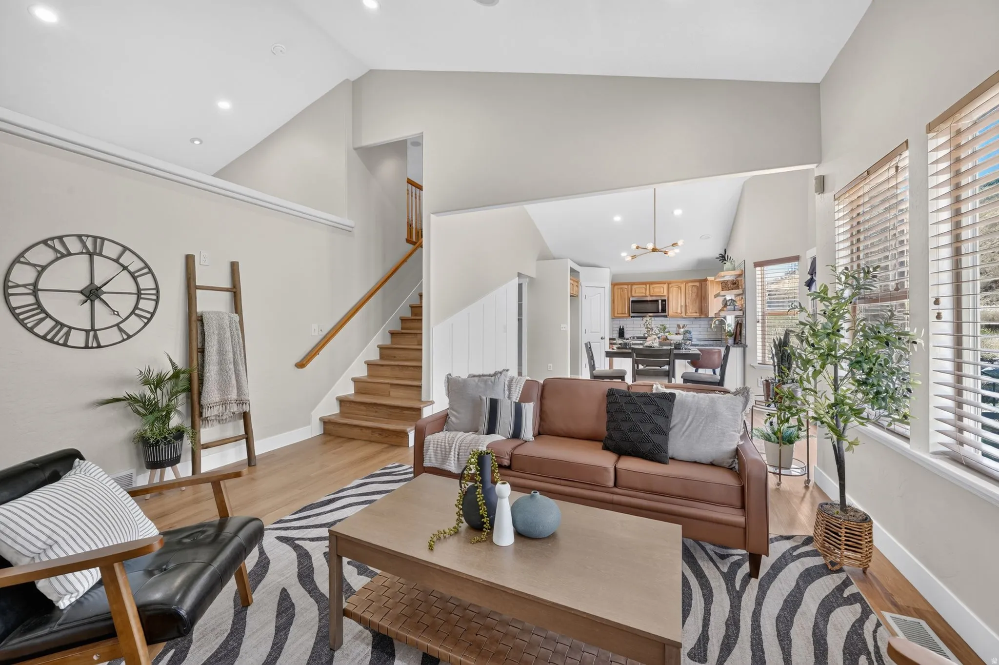 Vaulted ceilings, recessed lighting, wood-finish flooring, wood staircase with handrail, and multiple windows with blinds