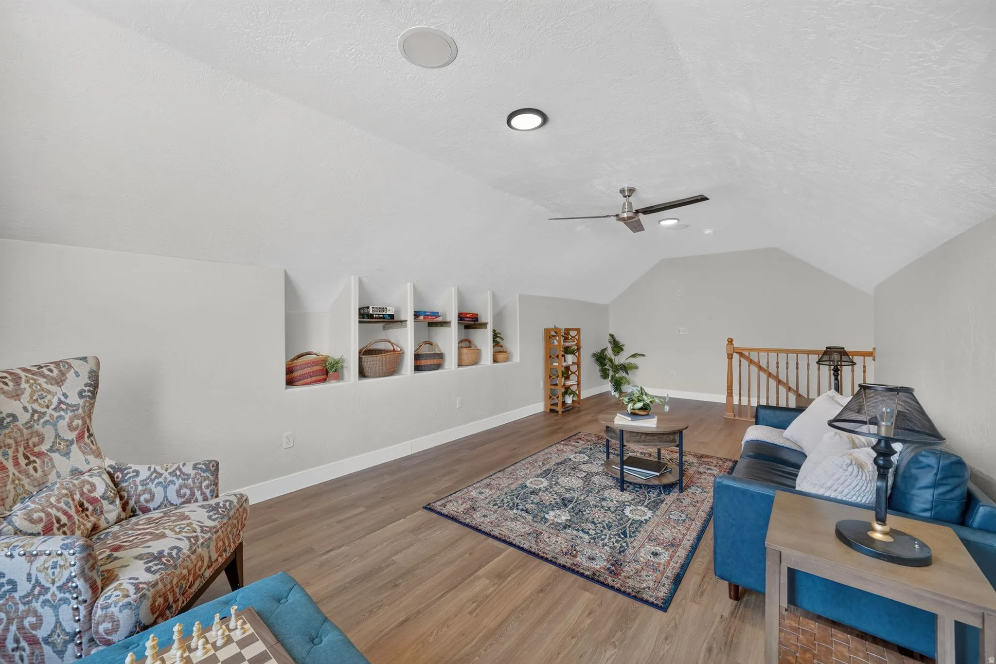 Sloped ceiling with recessed lighting and a ceiling fan, built-in shelving, wood-finish flooring, and a wood staircase with balusters