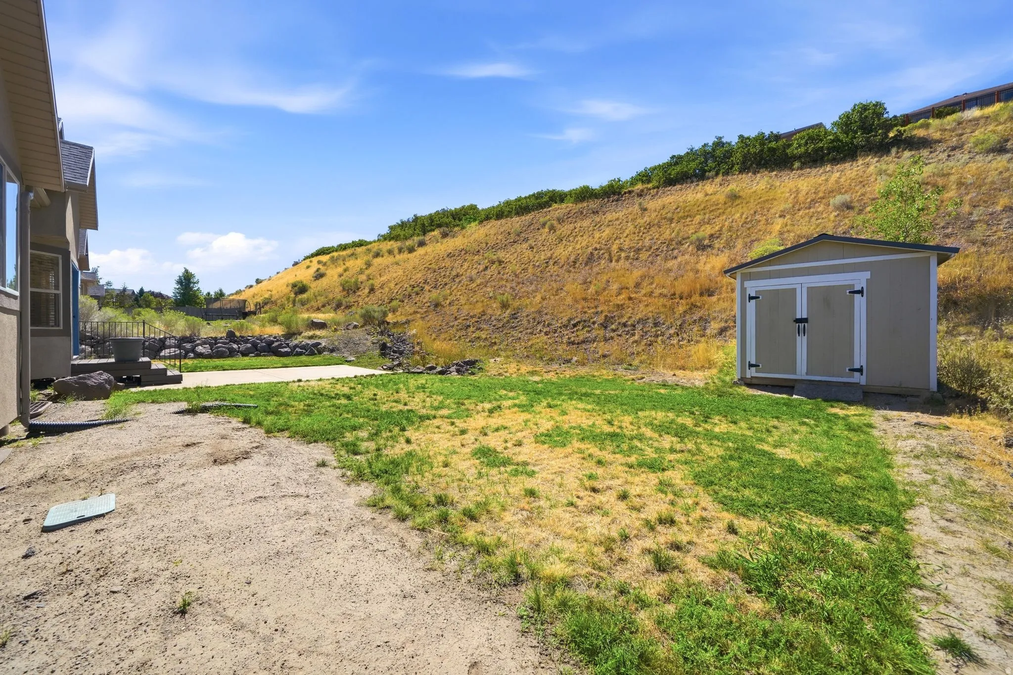 Expansive outdoor space featuring a detached storage shed, concrete patio, and sloped natural terrain