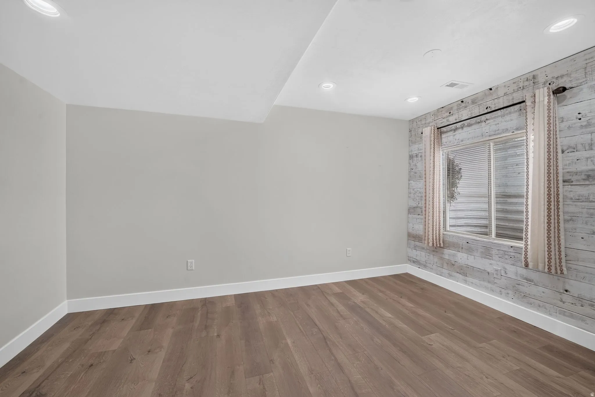 Wood-finish flooring, recessed lighting, and a window with a decorative wood-panel wall