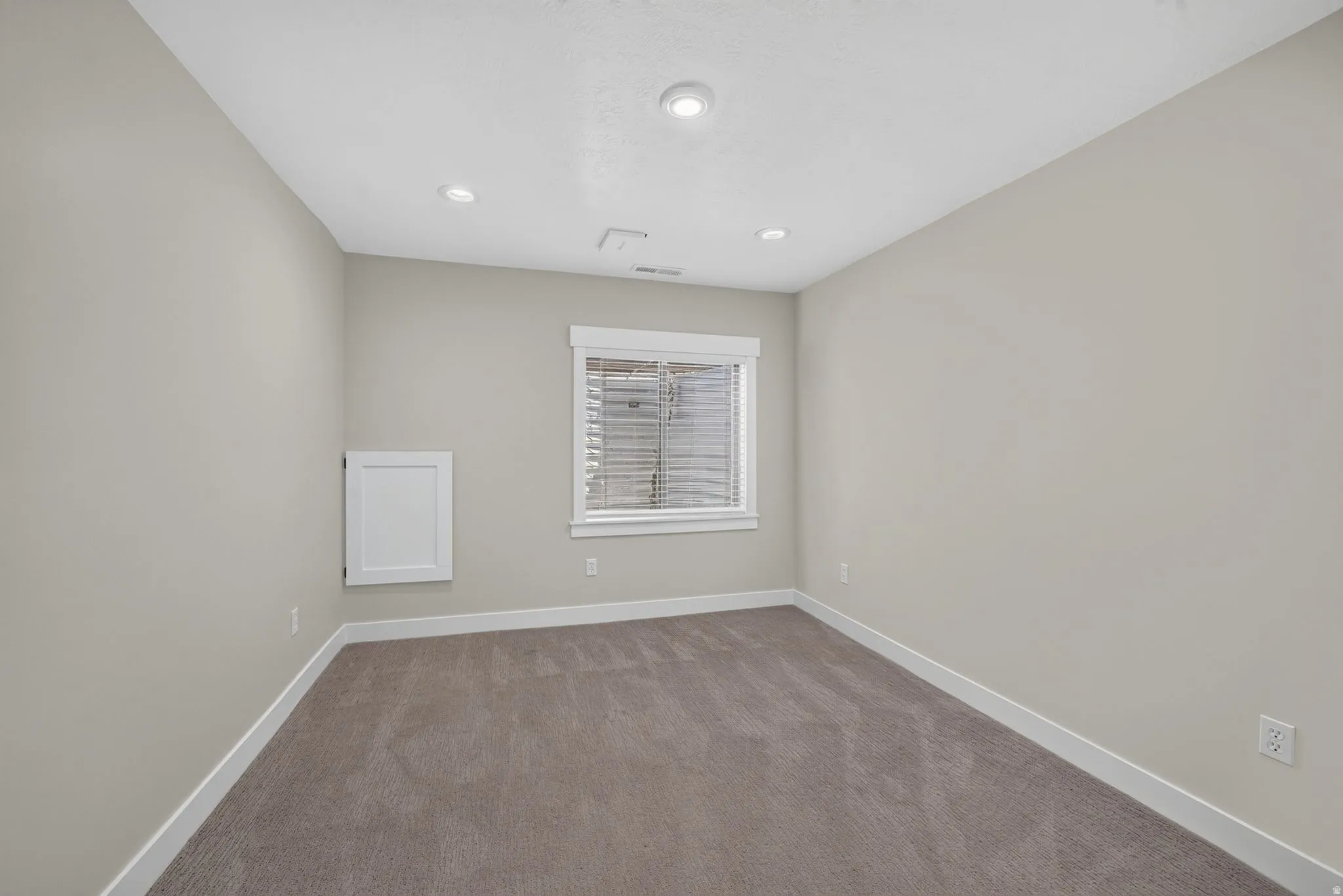 Recessed ceiling lighting, white trim, window with blinds, and neutral wall paint