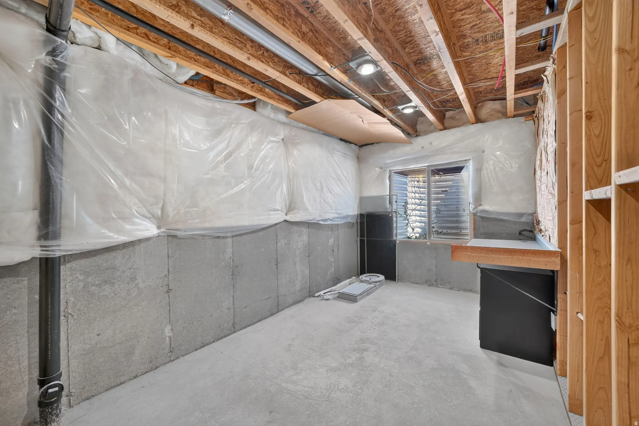 Unfinished basement with concrete slab flooring, exposed ceiling joists, recessed lighting fixtures, and a glass block window