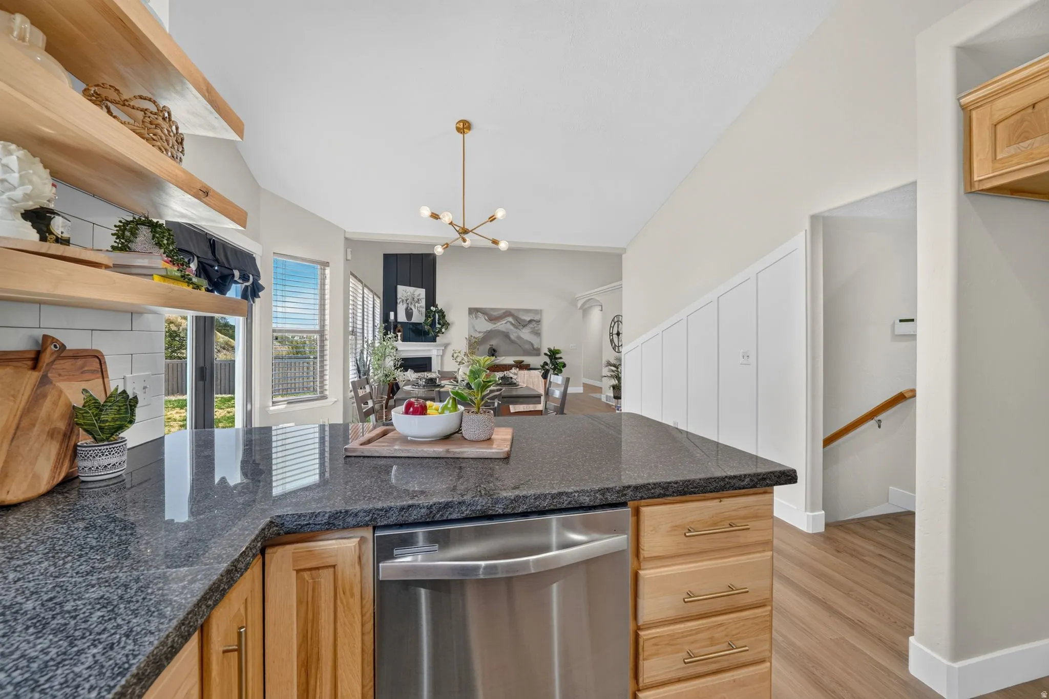 Kitchen island with a dark countertop, natural wood cabinetry, and a built-in stainless steel dishwasher
