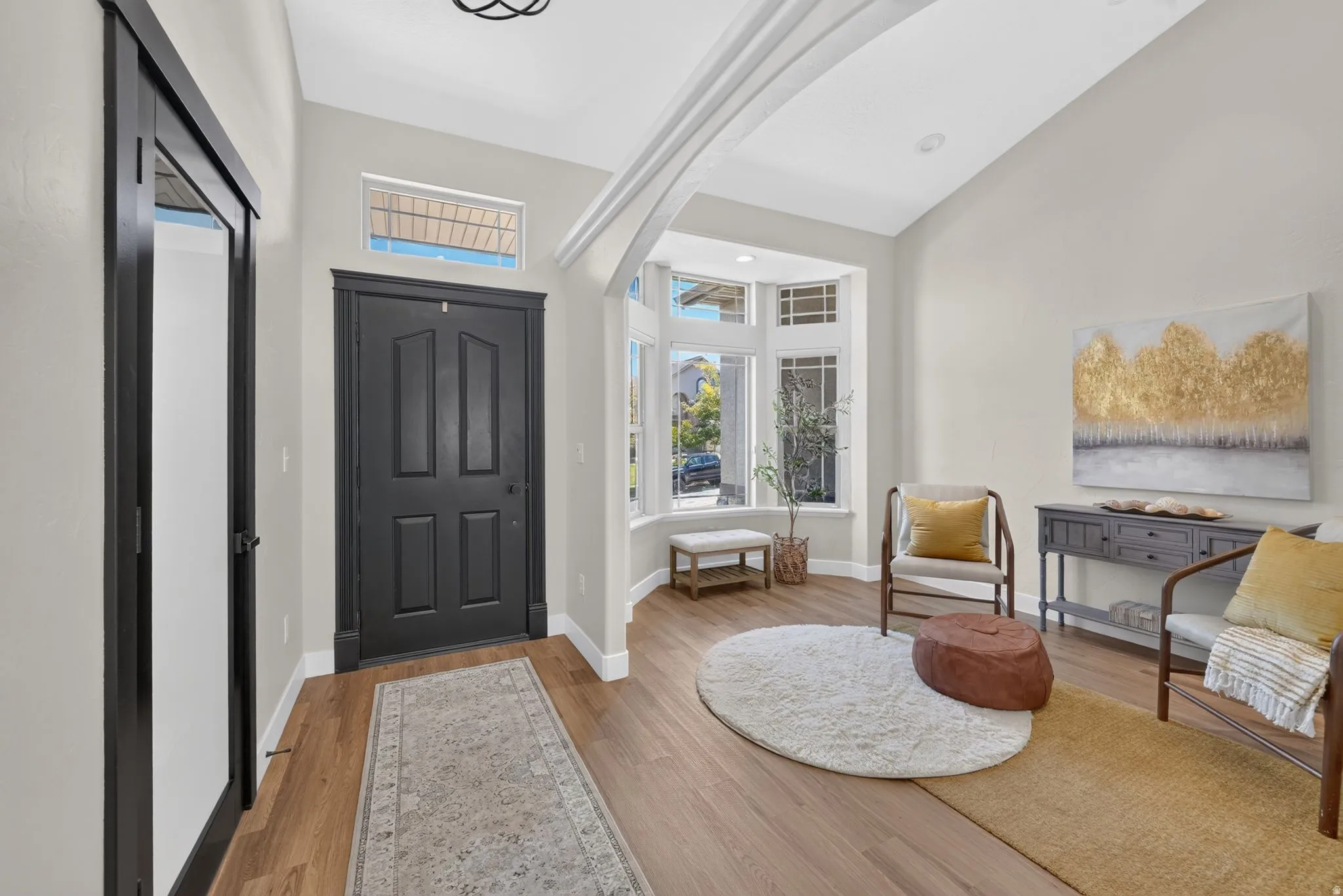 Entryway featuring a dark paneled door with transom window, wood-finish flooring, and a bay window with multiple panes