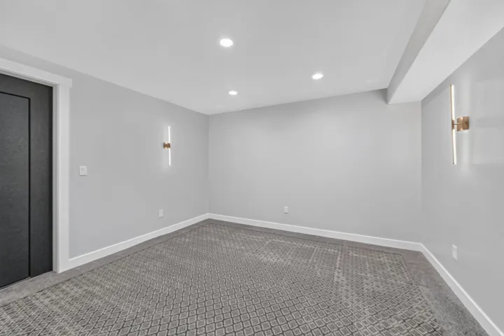 Recessed ceiling lighting, patterned carpeting, modern wall sconces, white trim, and a dark paneled door