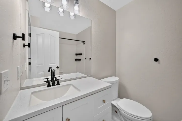 White vanity with integrated sink, black fixtures, and a large wall-mounted mirror