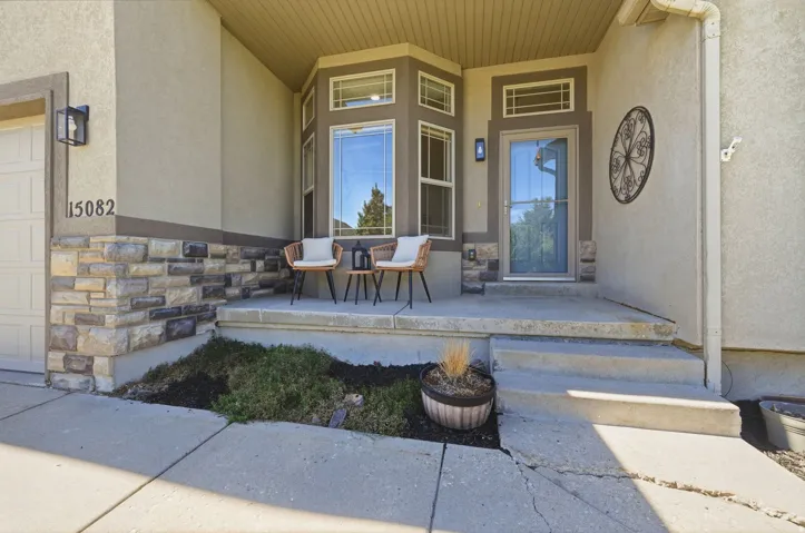 Stucco exterior with stone accent detailing, covered entryway, bay window with multiple panes, full-light entry door, and concrete steps
