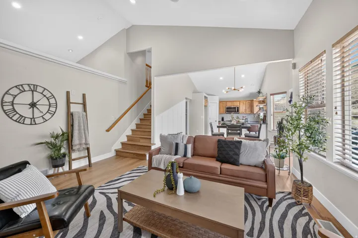 Vaulted ceilings, recessed lighting, wood-finish flooring, wood staircase with handrail, and multiple windows with blinds