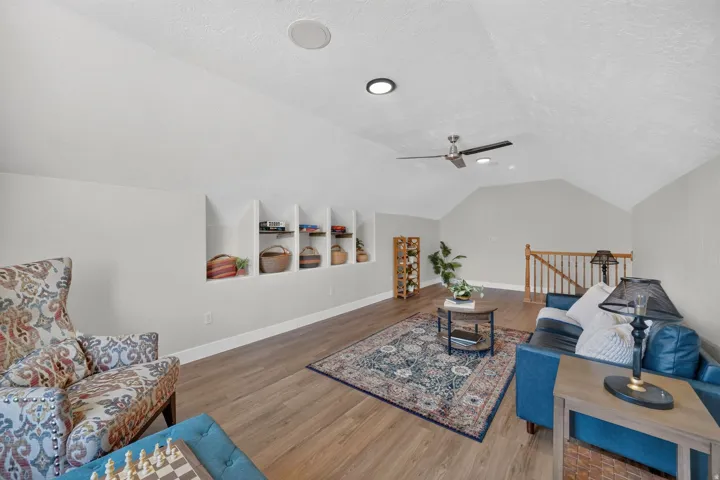 Sloped ceiling with recessed lighting and a ceiling fan, built-in shelving, wood-finish flooring, and a wood staircase with balusters