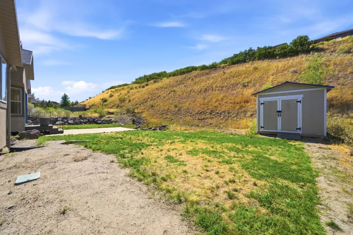 Expansive outdoor space featuring a detached storage shed, concrete patio, and sloped natural terrain