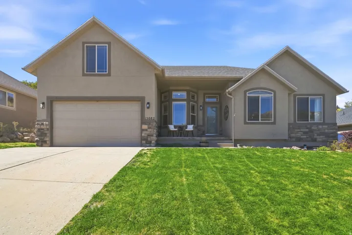 Stucco exterior featuring stone accents, an attached garage, a concrete driveway, and a covered entry porch