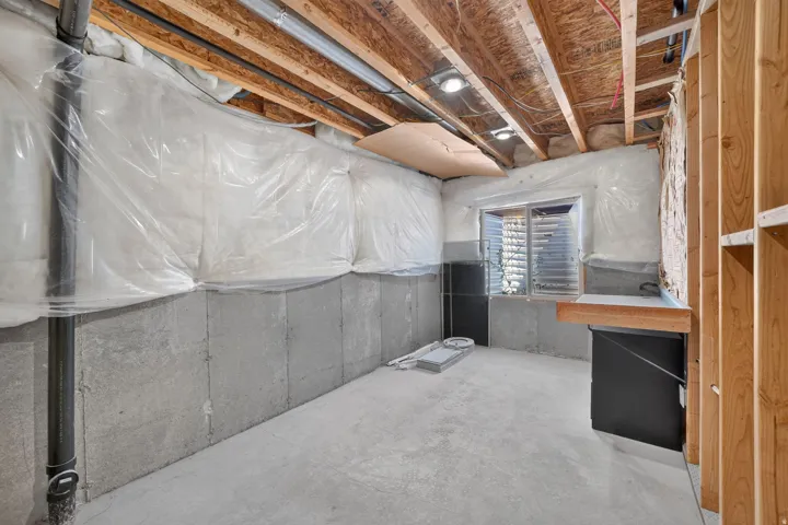 Unfinished basement with concrete slab flooring, exposed ceiling joists, recessed lighting fixtures, and a glass block window