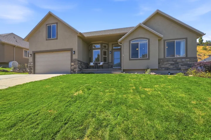 Stucco exterior with stone veneer accents, multi-pane windows, attached garage, and a tiered front lawn